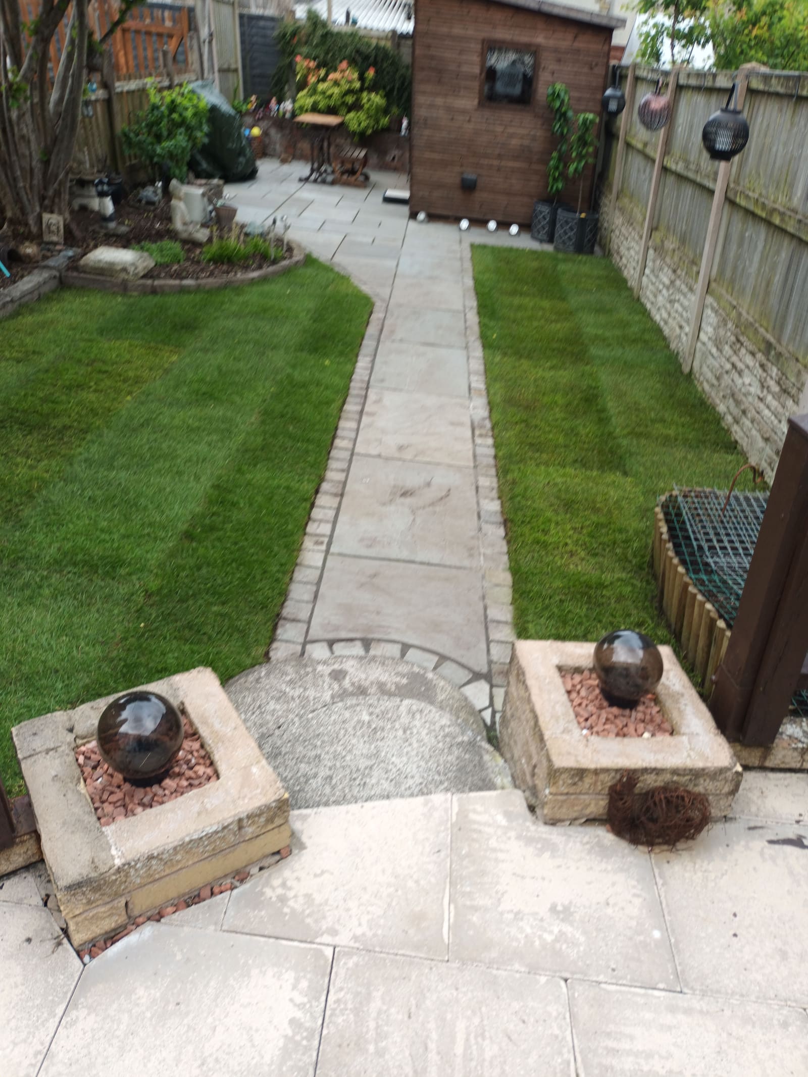 Landscaped garden with stone patio pathway, striped lawn and water feature ornaments